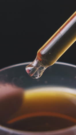 person puts glass pipette into cup with light brown liquid on dark background extreme close view
