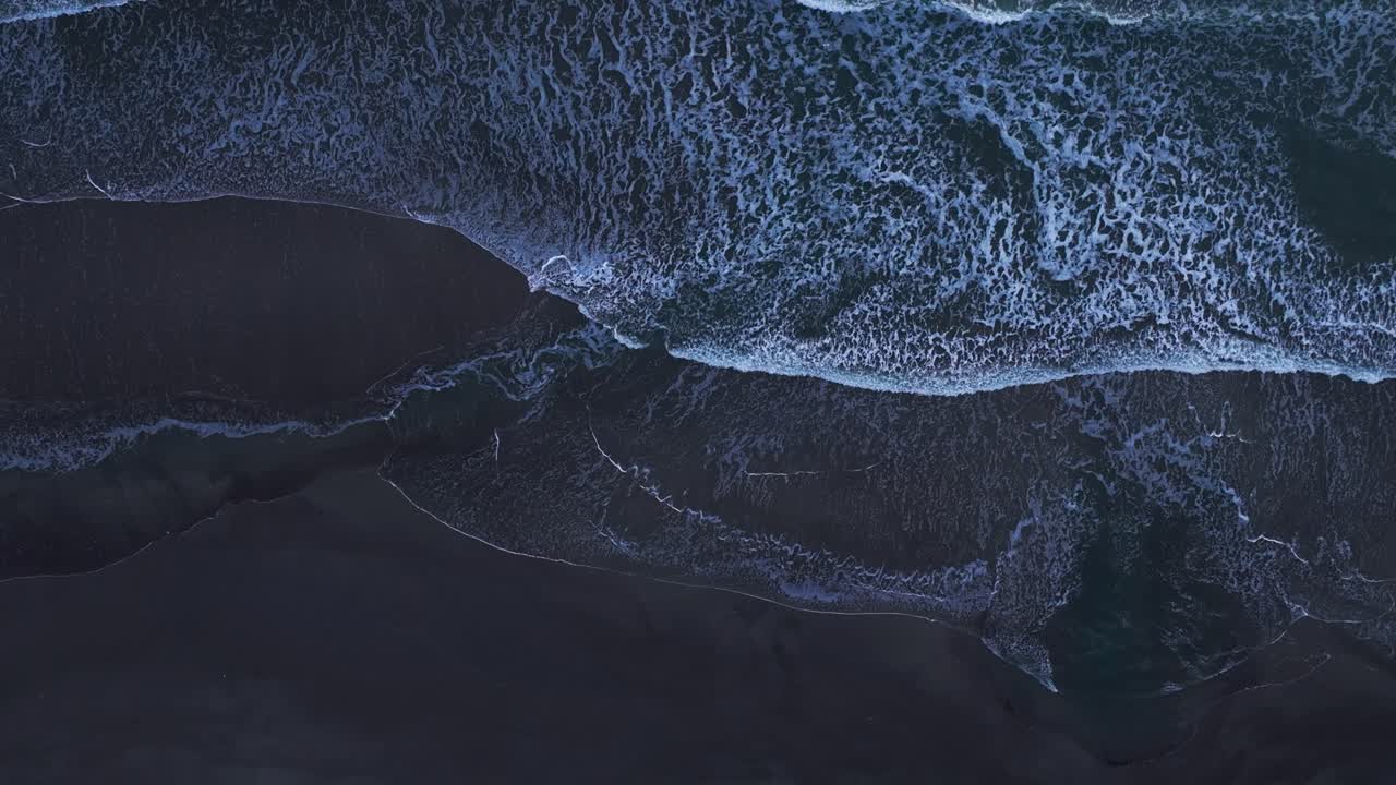 Drone aerial view looking straight down over white waves crashing on a beach