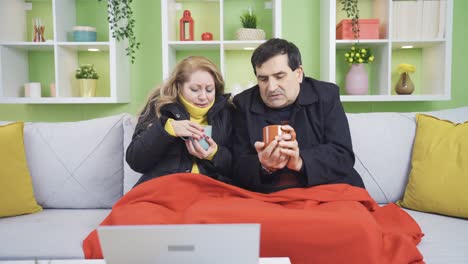 Mature-couple-trying-to-warm-up-with-hot-drink-due-to-cold.