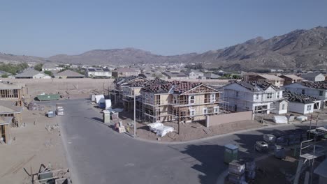 A-drone-gracefully-pulls-out-from-a-partially-built-house-on-a-construction-site,-revealing-the-entirety-of-the-construction-site-and-the-completed-homes-in-the-surrounding-area