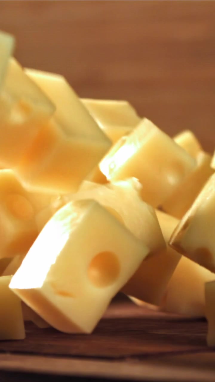 Gros plan au ralenti de dés de fromage tombant sur une surface en bois