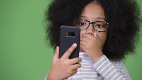 young cute african girl with afro hair looking shocked while using phone