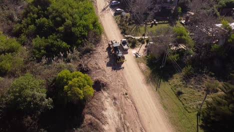 Yellow-tractor-machine-with-crane-working-on-construction-of-new-road-in-residential-area-of-Uruguay-in-neighborhood-of-Punta-del-Este