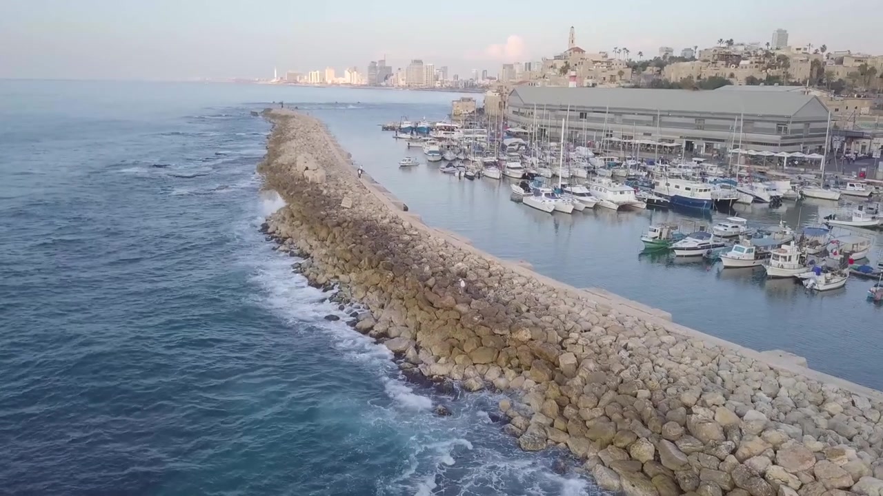 Le acque blu profonde del Mediterraneo si infrangono dolcemente sulla diga foranea mentre gli skyline al tramonto di Jaffa e Tel Aviv creano un bellissimo contrasto