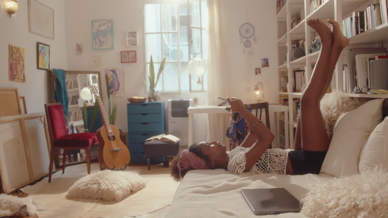 Relaxed Girl Lying with Legs Up on Bed and Using Smartphone at Home