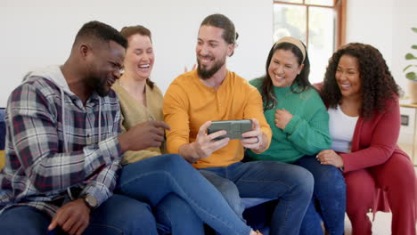 Happy-diverse-male-and-female-friends-relaxing-at-home-together-talking-and-looking-at-smartphone