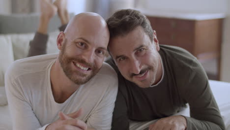 cheerful homosexual men lying on bed and smiling at camera