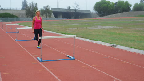 side view of caucasian female athlete jumping over hurdle on race track 4k