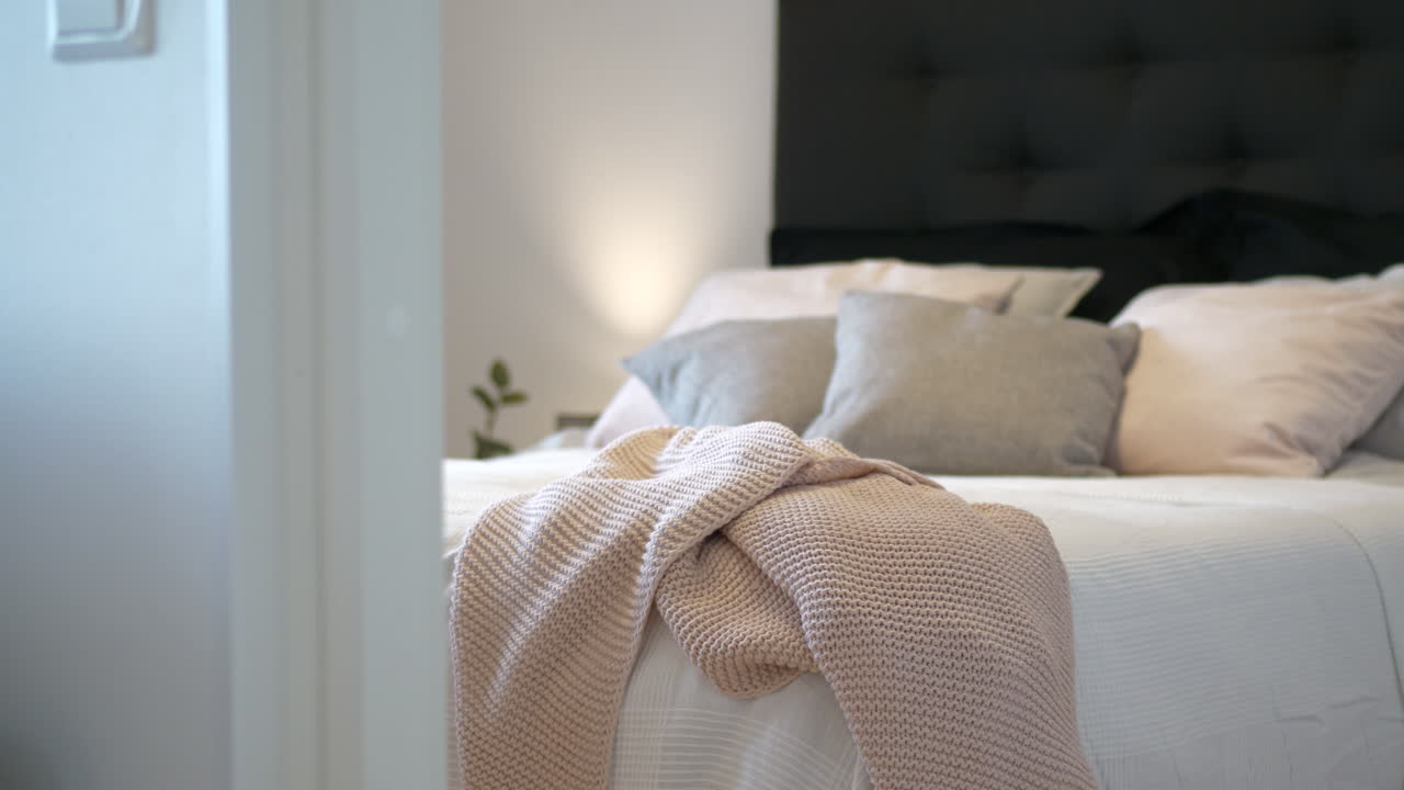 Ripresa a scorrimento lento attraverso la porta di una moderna camera da letto luminosa, cuscini sul letto
