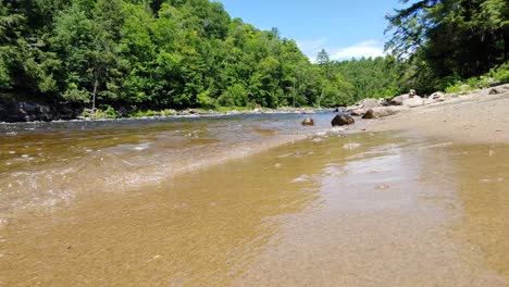 Primer-Plano-En-ángulo-Bajo-De-Las-Olas-Naturales-Del-Río-Salpicando-En-La-Orilla-Arenosa-Durante-Un-Hermoso-Día-Soleado-En-La-Naturaleza