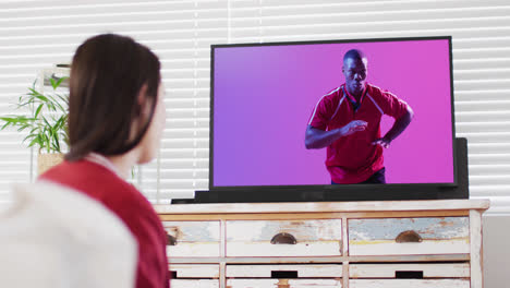 mujer caucásica viendo la televisión con un jugador de rugby afroamericano atrapando la pelota en la pantalla