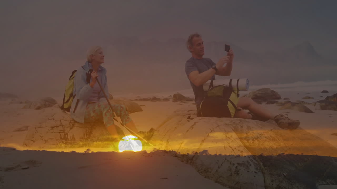 Couple hiking on sunset beach, using smartphone and trekking pole for travel content creation