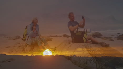 couple hiking on sunset beach, using smartphone and trekking pole for travel content creation