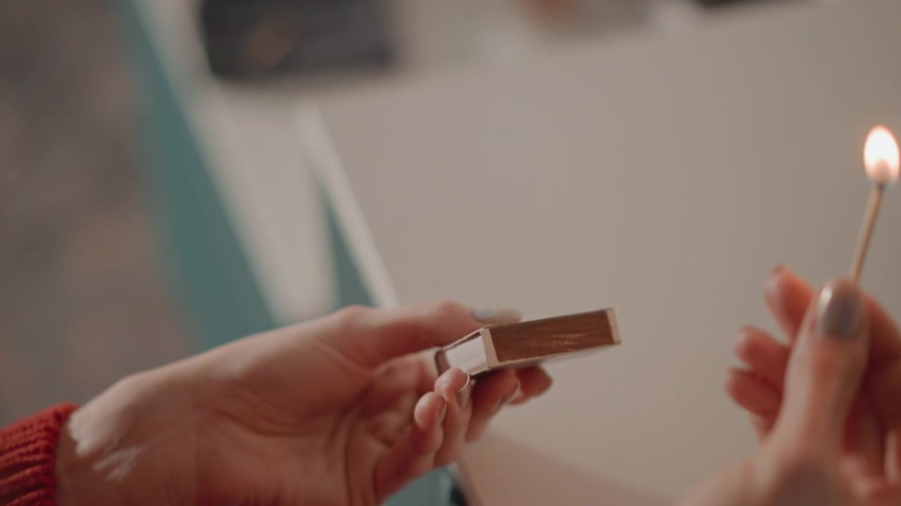 İki elin yakın iç mekan görünümü, küçük metal plastik bir parçayı yanmış bir kibritle dikkatlice ısıtıyor, parlak bir mandalın yakınında sabit bir tutuşla tutarken, hafif bir parıltı ve hafif duman onarım, test ve hassas bir işlemi düşündürüyor.