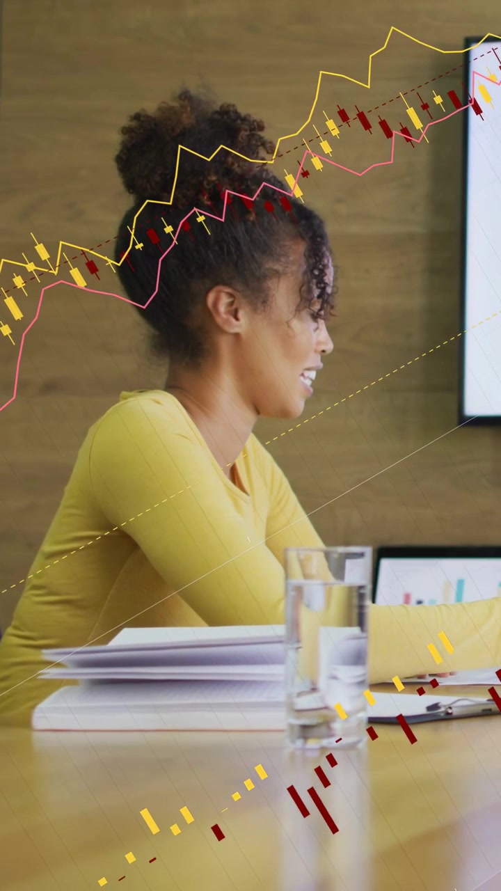 Vertical video: Leaning woman yellow top discussing at meeting table as charts animating on laptop