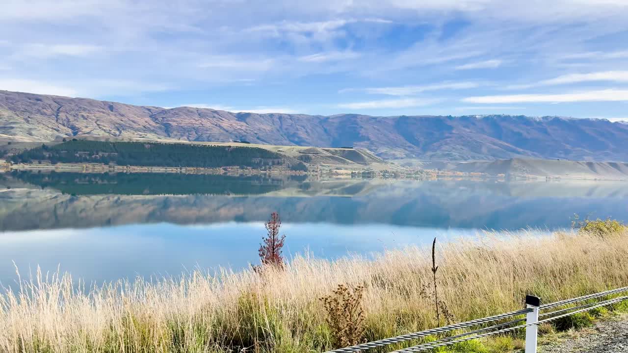 A serene drive by a tranquil lake with mountain reflections under a clear sky in Queenstown, New Zealand