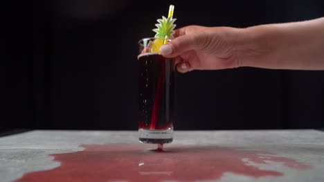 woman picking up red cocktail with pineapple décor from messy table