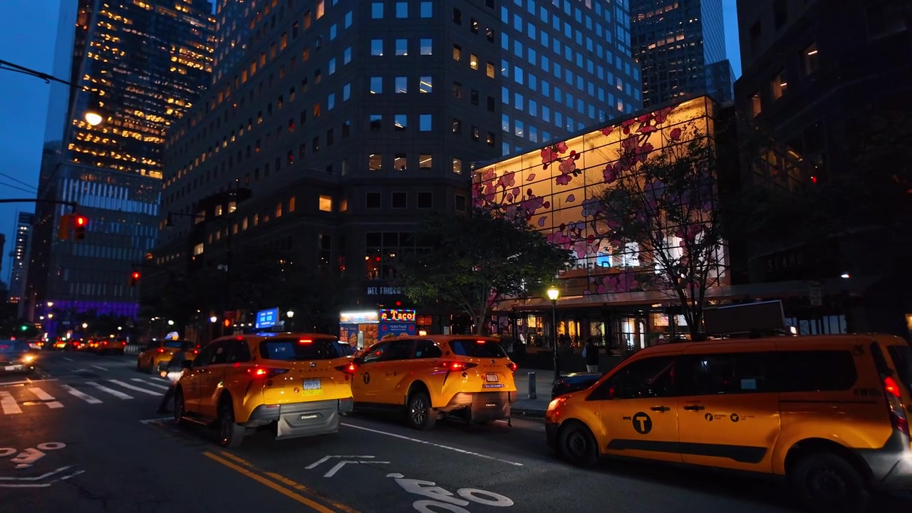 New York, USA, 5 June 2026 : Yellow taxis at Brookfield Place, New York City, New York. Street level traffic beside illuminated floral storefront panels and office towers at blue hour.