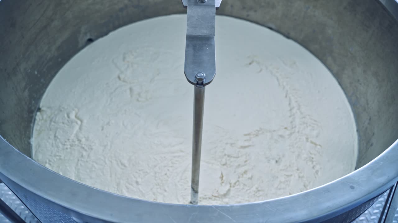 Factory equipment close-up. Metal mixing apparatus boils and mix milk for making cheese at milk products making factory in slow motion.