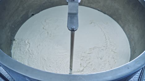 factory equipment close-up. metal mixing apparatus boils and mix milk for making cheese at milk products making factory in slow motion.