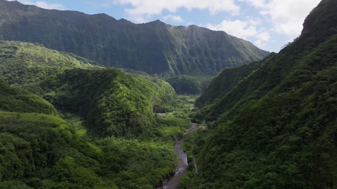 Drönarvyer över regnskogen på ön Tahiti under en dag med växlande molnighet. En flod flyter genom ravinen mellan Tahitis berg.