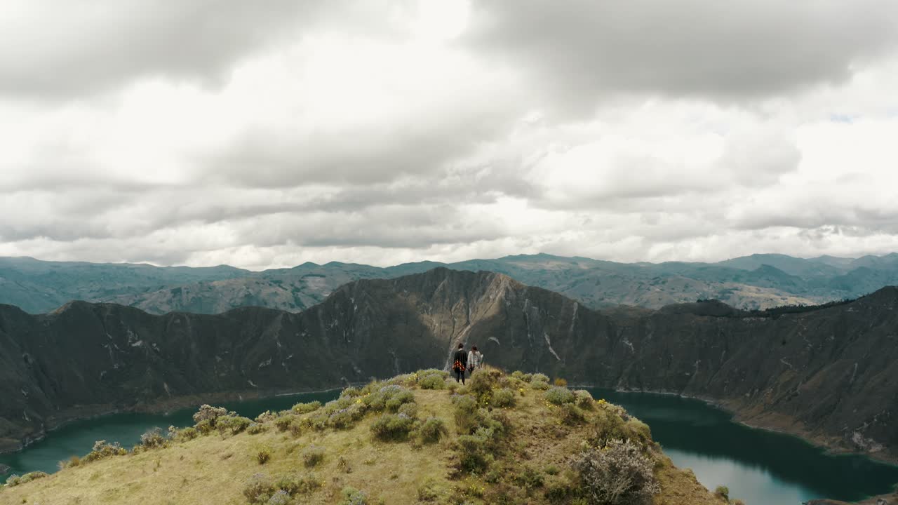 toma de seguimiento ascendente de una pareja parada en la cima de una montaña y disfrutando de la vista del lago del cráter del volcán durante el día nublado