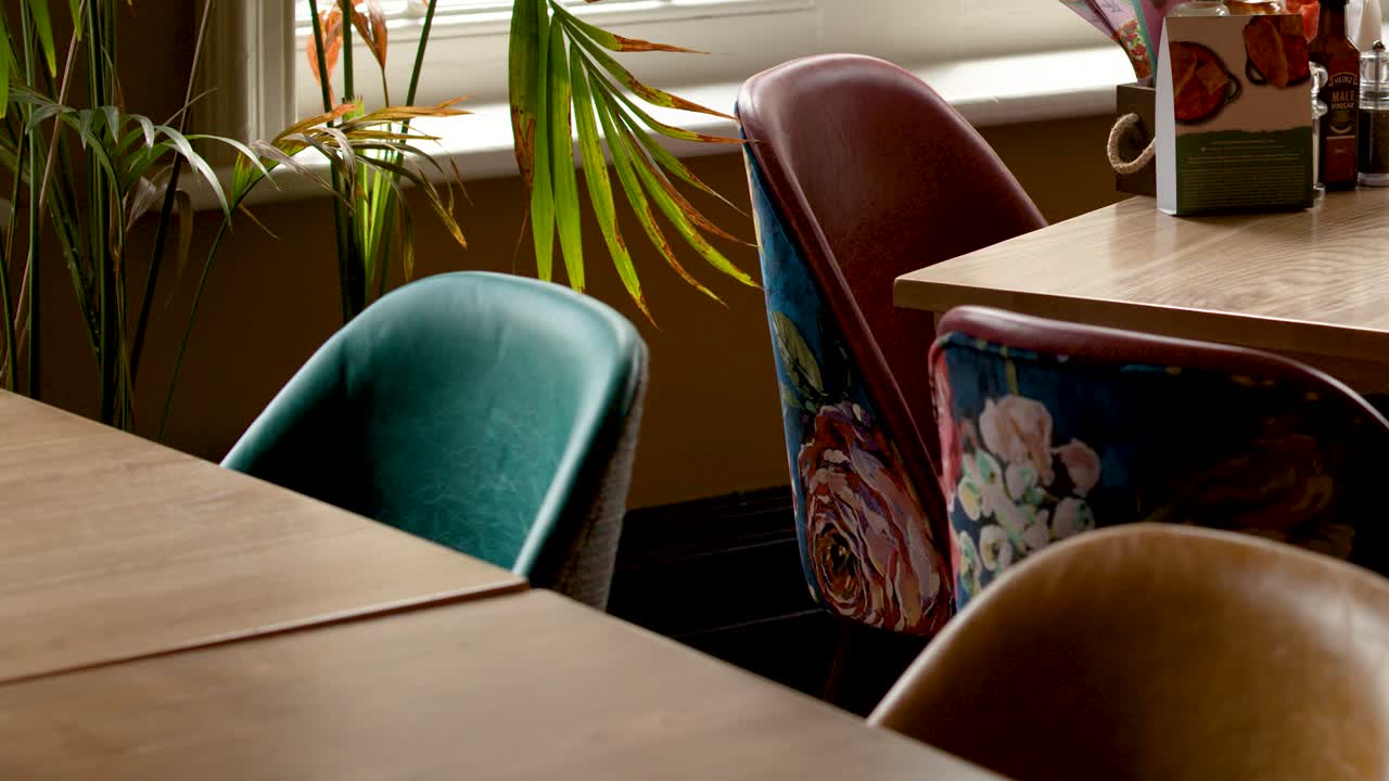 Camera slowly pans over colorful retro chairs and wooden tables in warmly lit vintage cafe