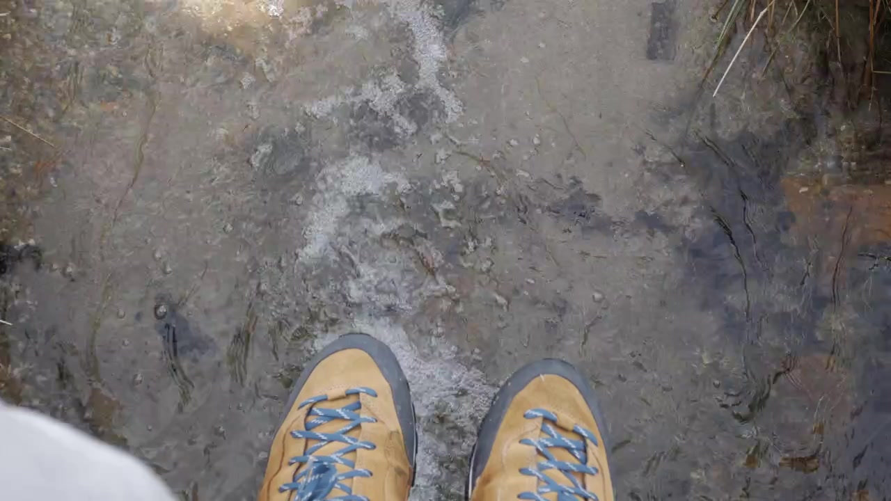 Boots standing in shallow, clear stream with visible current and wet, rocky bottom