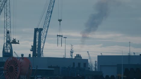 Slowmotion-dolly-shot-alongside-a-shipyard-with-smoke-rising-from-a-large-cruise-ship