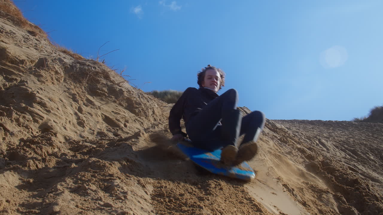 niño feliz se desliza por una duna de arena en un trineo