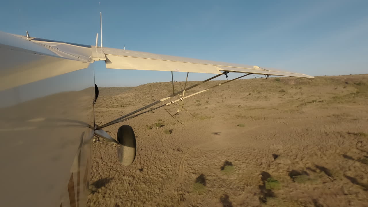 Kleines Flugzeug in Seitenansicht fliegt tief über Sträuchern und Hügeln