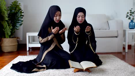 young muslim woman and female friend reading quran and praying