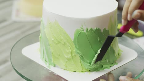 de cerca, el chef está esparciendo crema verde pastel alrededor del pastel.