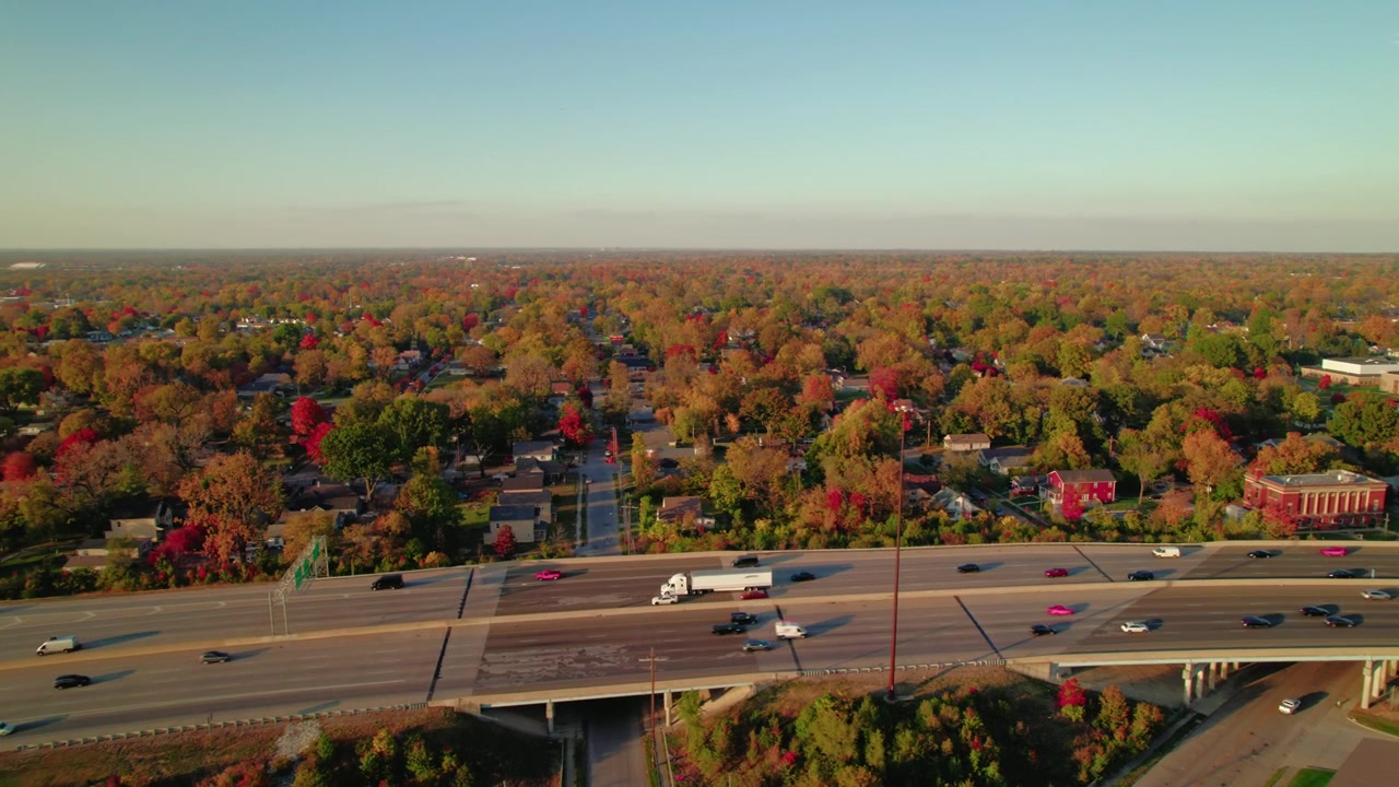 Inseguimento di un semirimorchio furgonato sulla I-70 a Indianapolis, Indiana, con case suburbane e fogliame autunnale sullo sfondo.