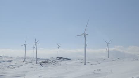 panning down on massive wind turbines spinning in a snowy alpine mountain range on a sunny day. indicating clean energy projects, sustainability campaigns, or environmental infrastructure.
