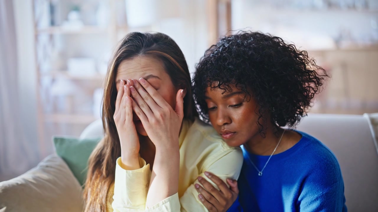 Mulher confortando amiga triste no sofá. Amigas multirraciais apoio emocional em casa