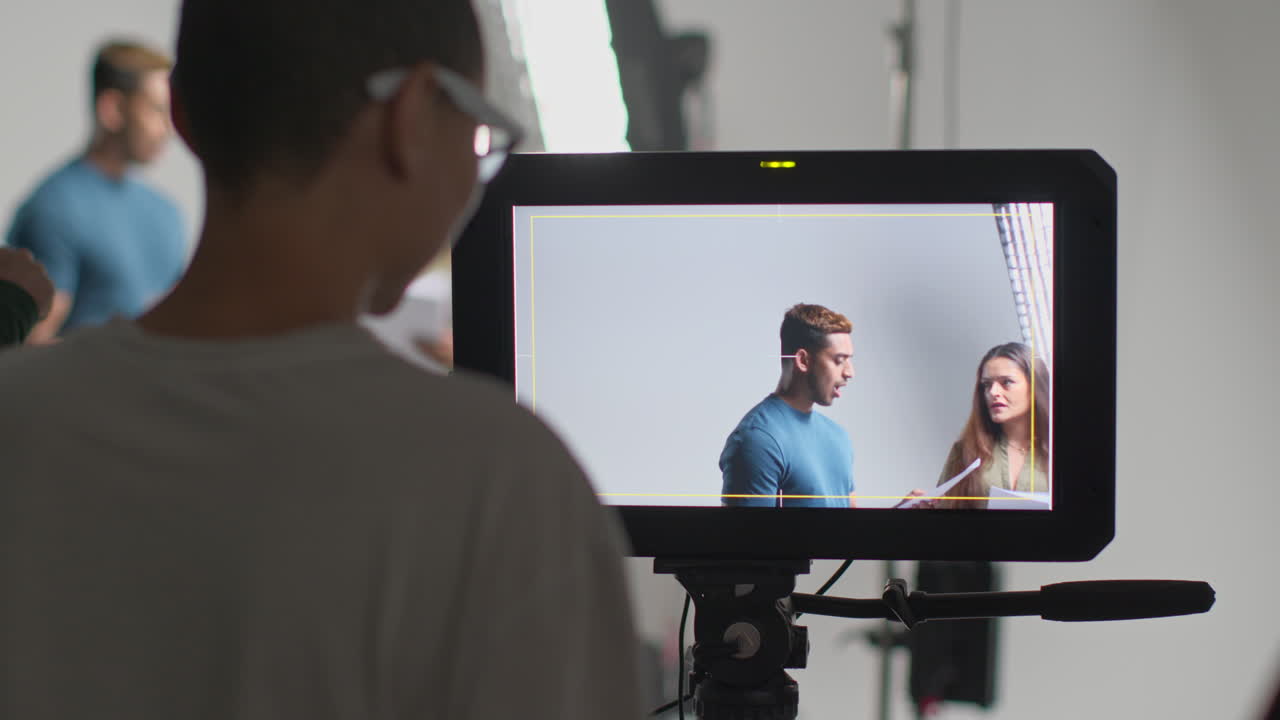 режиссер фильма смотрит на мужских и женских актеров, держащих сценарии, репетирующих для съемок фильма или видео в студии на мониторе 1