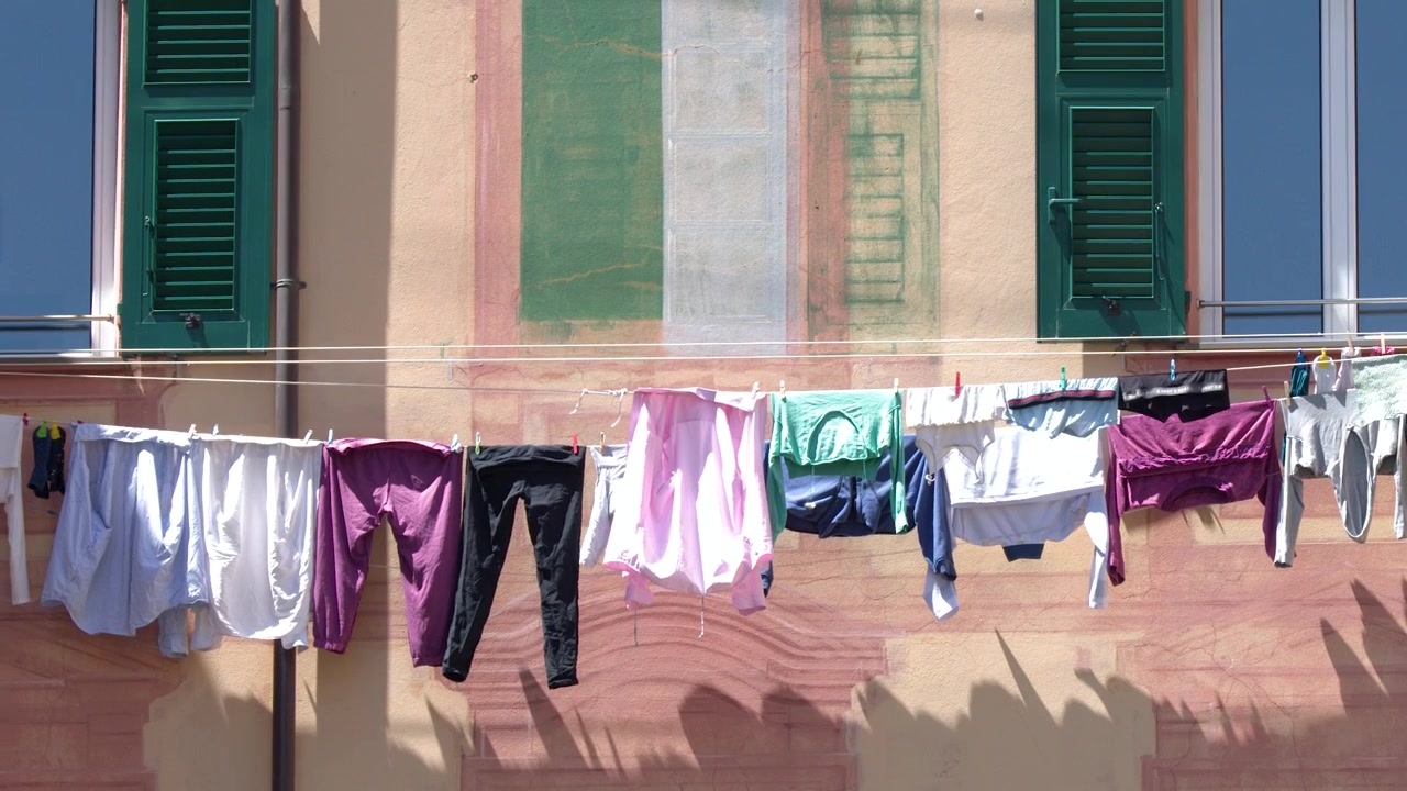 Static shot of colorful laundry drying on a clothesline against a pink Mediterranean building facade.