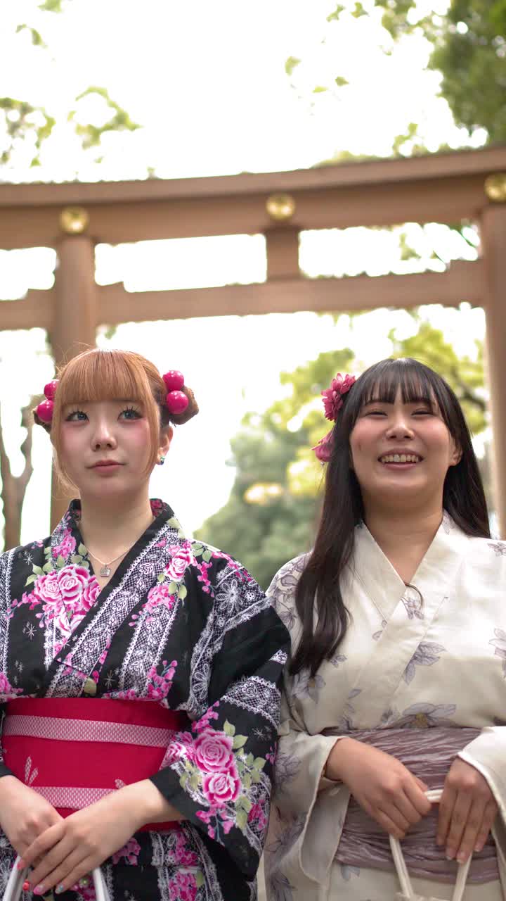 Lavvinkelbilde av to kvinner iført blomstrete yukataer som smiler ved en Shinto-helligdom.