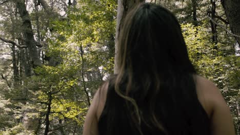 a camera from behind of a woman looking up to the trees, relaxing and breathing at the forest