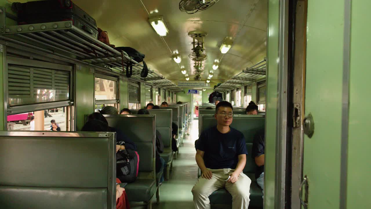 Interior of old commuter train in Bangkok with seated passengers, handheld camera moving through carriage
