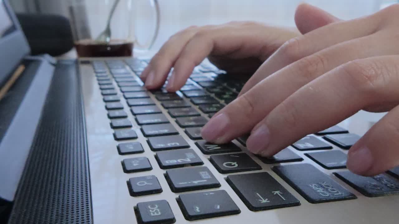 Side angle of a female student's hands typing lecture notes or research on a laptop