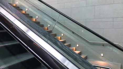 view from the first person on an escalator looking to the stairs along the escalator at a building