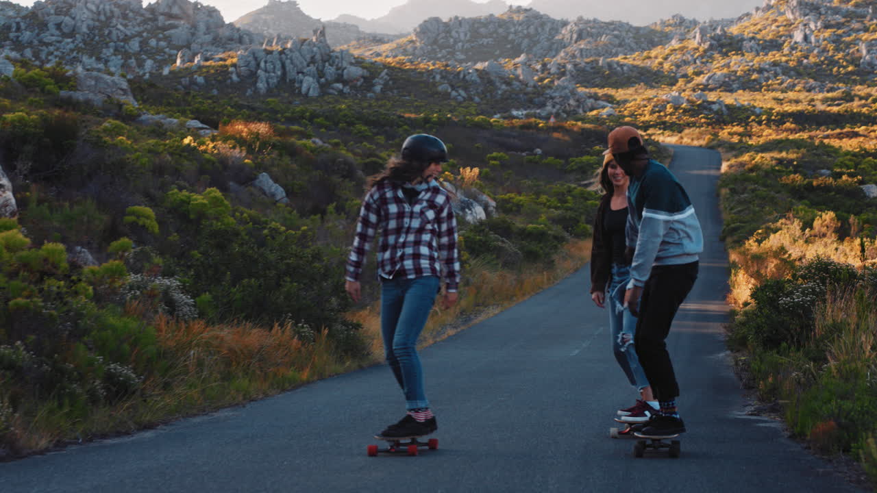felices amigos multiétnicos longboarding juntos montando patineta crucero en la carretera del campo divirtiéndose pasar el rato disfrutando de unas vacaciones de verano relajadas