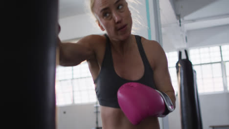 boxeadora caucásica con guantes de boxeo entrenando con saco de boxear en el gimnasio