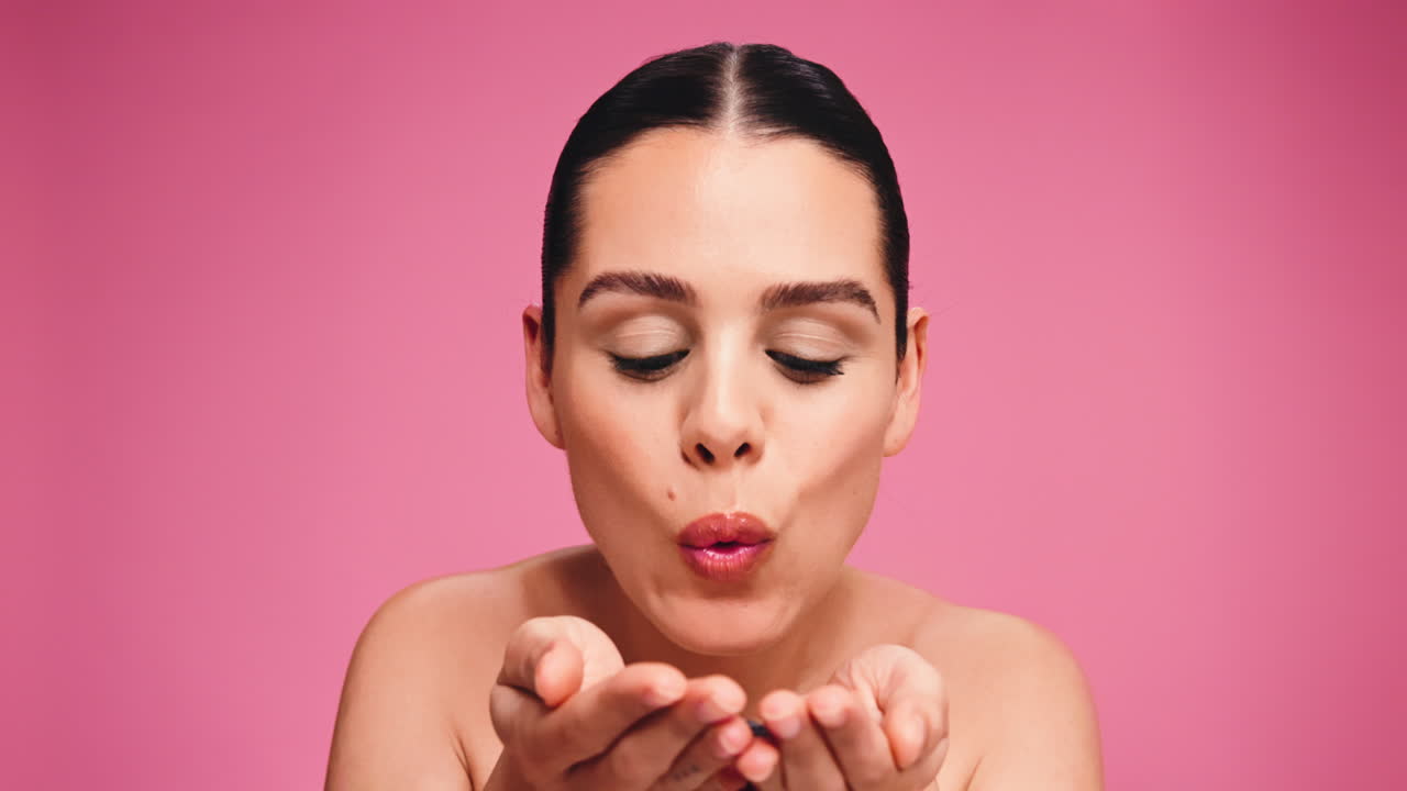 Woman blowing confetti on pink background