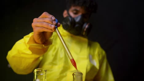 científico con traje de hazmat amarillo que arroja sangre en tubos de laboratorio para análisis y estudios de infección y reacción de virus, químico con máscara respiratoria que trabaja en laboratorio de fondo negro oscuro