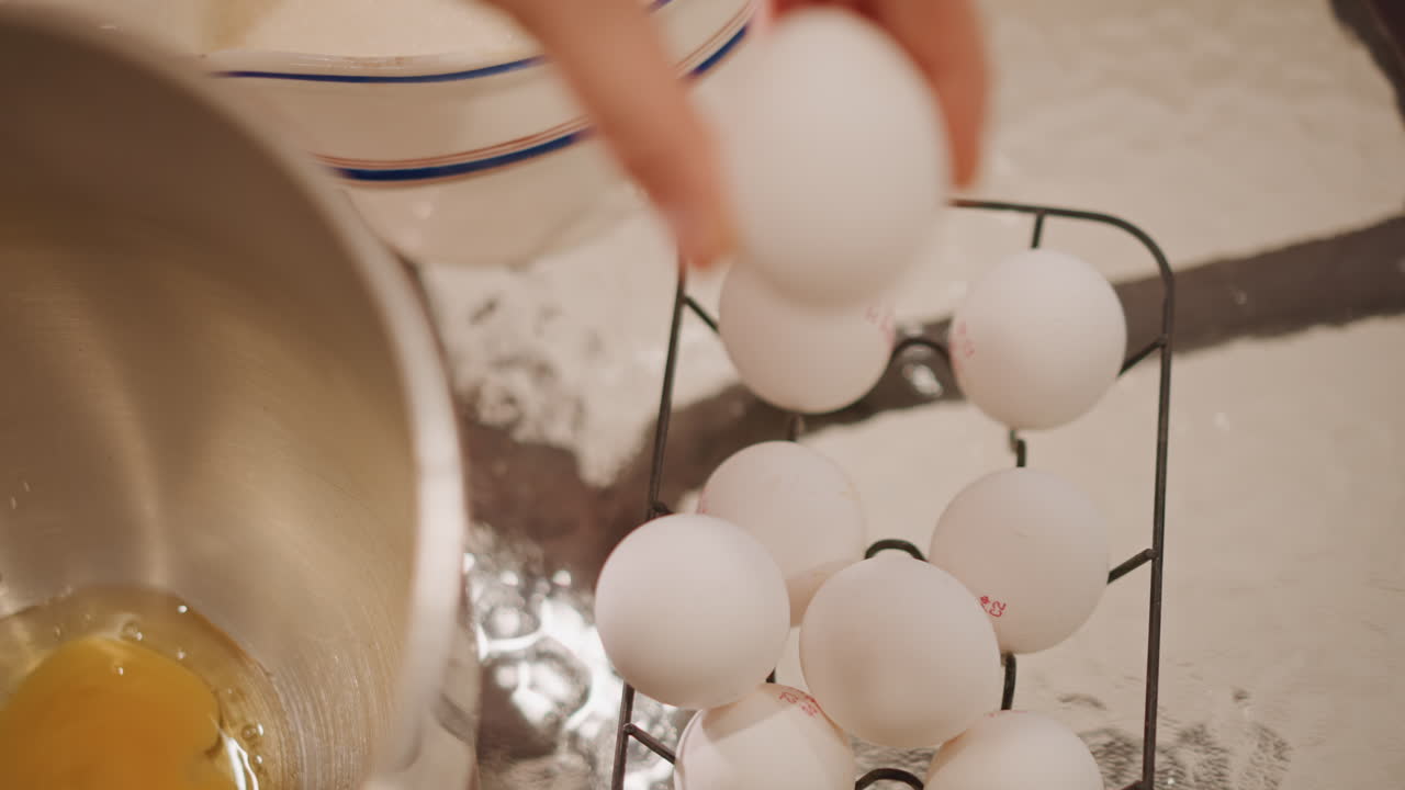 Overhead white eggs near mixing bowl as family matriarch cracks eggs for pumpkin pie, vintage ceramic jug and stainless bowl, amber yolks pooling, slow deliberate motions, sentimental warm kitchen