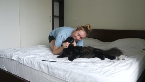 Content-furry-black-cat-sprawled-on-bed-together-with-happy-female-owner