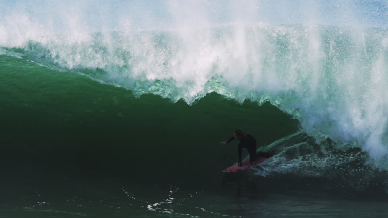 Slow motion shot of surfer engulfed in frothy green wave inside deep barreling tube